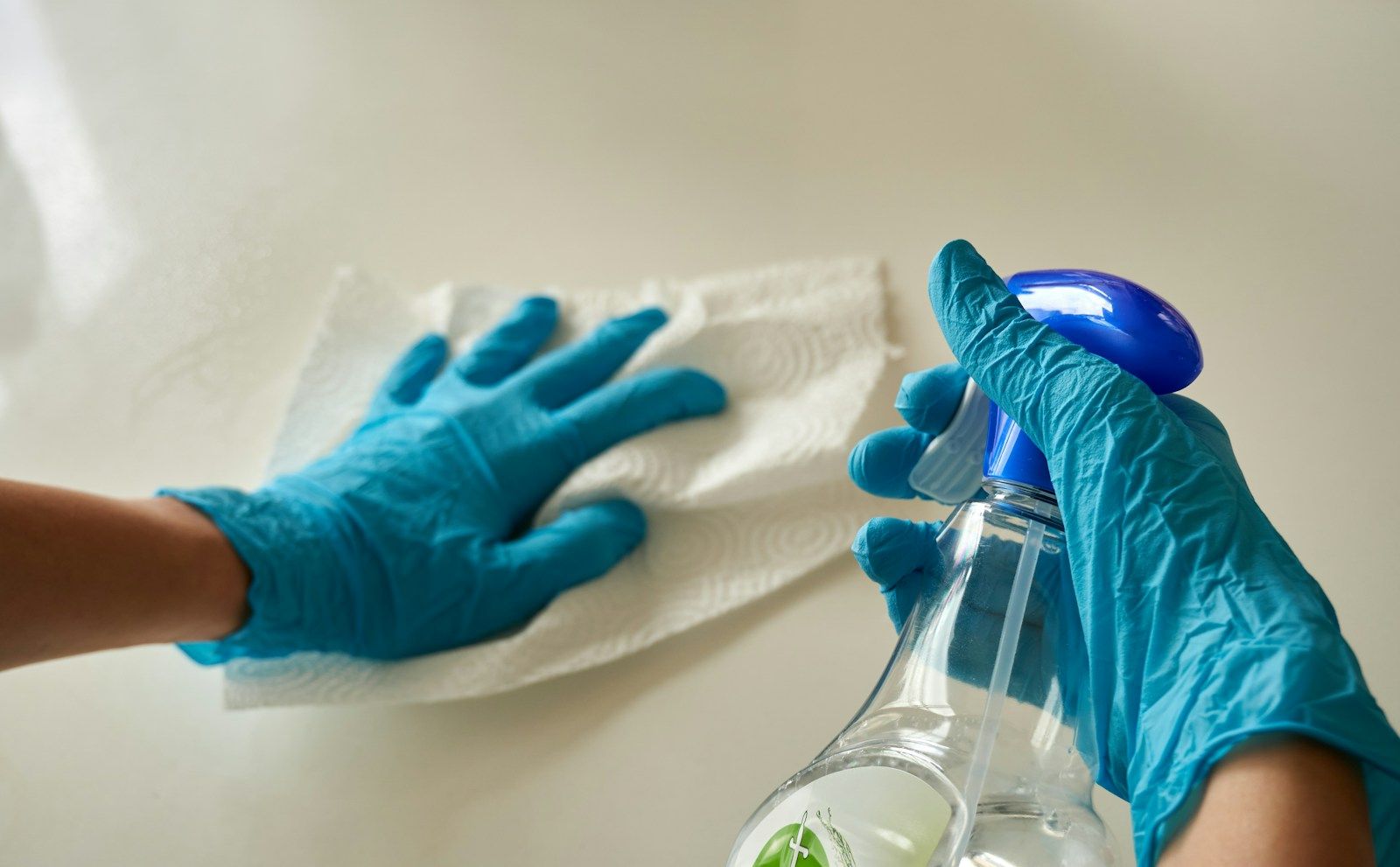 Gloved hands wiping down a countertop with a cloth and spray bottle